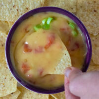 hand dipping a chip into vegan queso