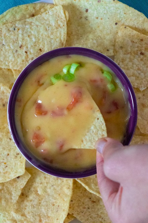 close-up of a hand dipping a chip into a bowl of vegan queso