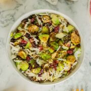 warm brussels sprouts salad in a serving bowl with lemons and dressing on the table next to it