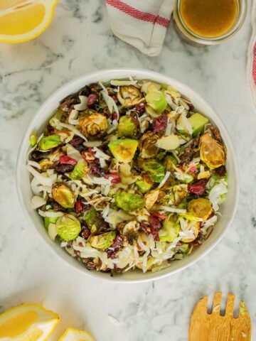 warm brussels sprouts salad in a serving bowl with lemons and dressing on the table next to it