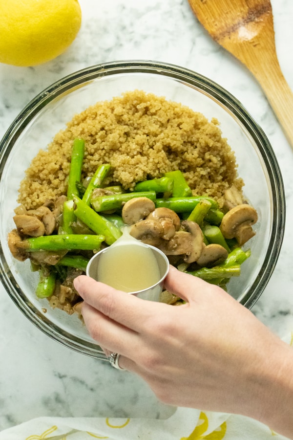 hand pouring lemon juice into a bowl of quinoa, asparagus, and mushrooms
