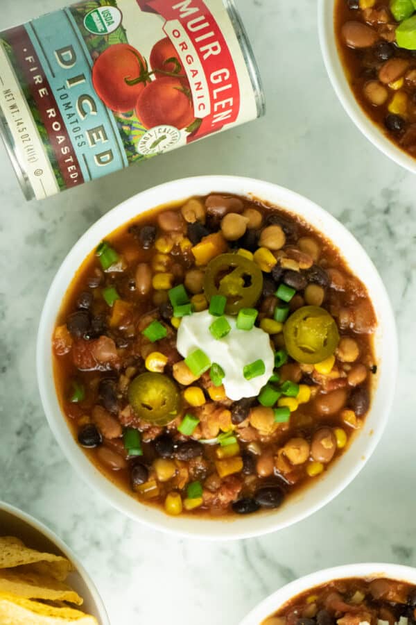 A bowl of vegan 3-bean chili topped with pickled jalapenos, vegan sour cream, and chopped green onion