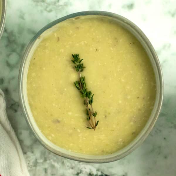 bowl of potato leek soup on a marble tabletop with a piece of fresh thyme as garnish