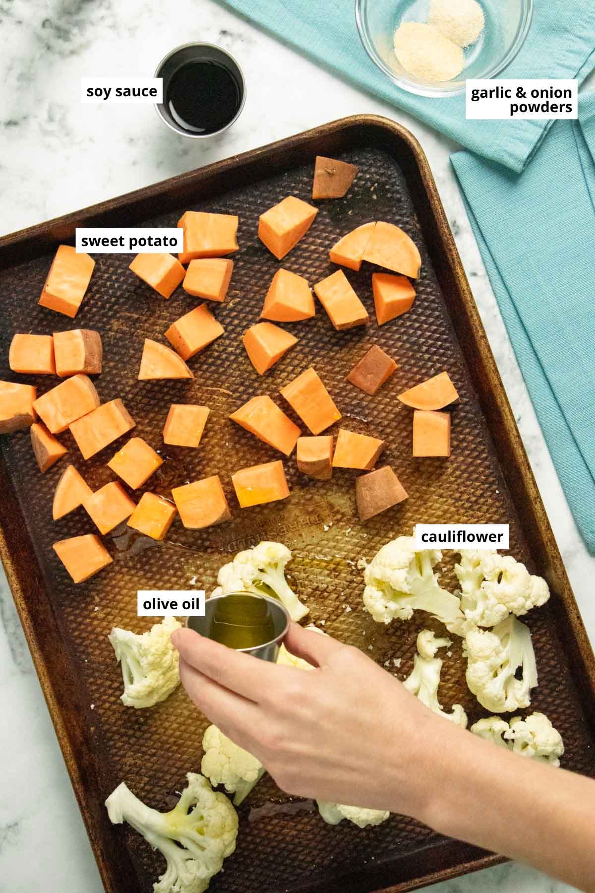 adding olive oil to cauliflower and sweet potato on a sheet pan