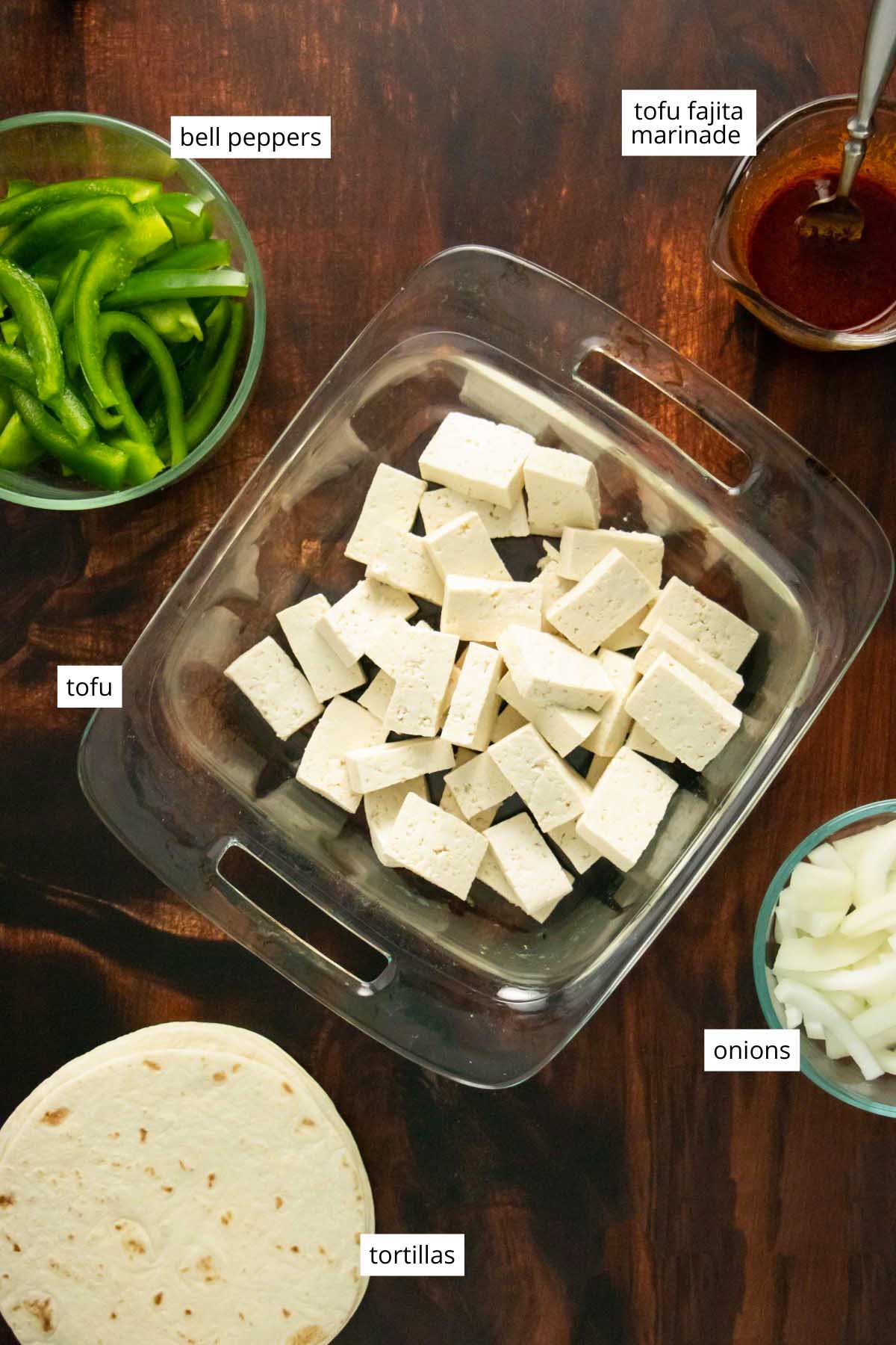tofu, veggies, tortillas, and the tofu fajitas marinade in containers on a wooden table