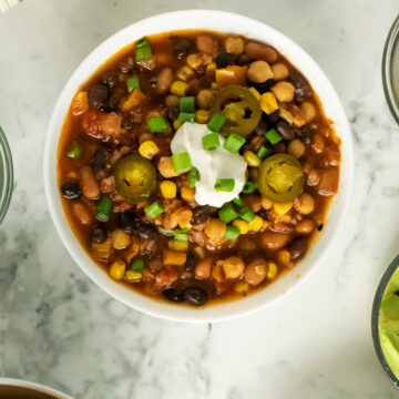 vegan bean chili topped with vegan sour cream, green onion, and jalapeno in a white bowl on a marble table