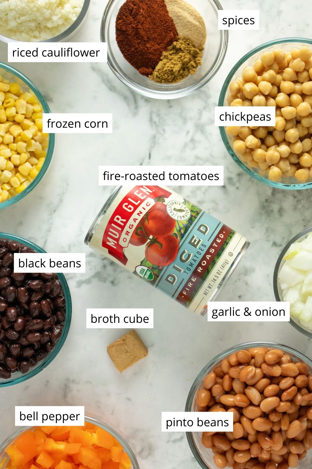 canned tomatoes, beans, and other chili ingredients on a marble table with text labels for each ingredient