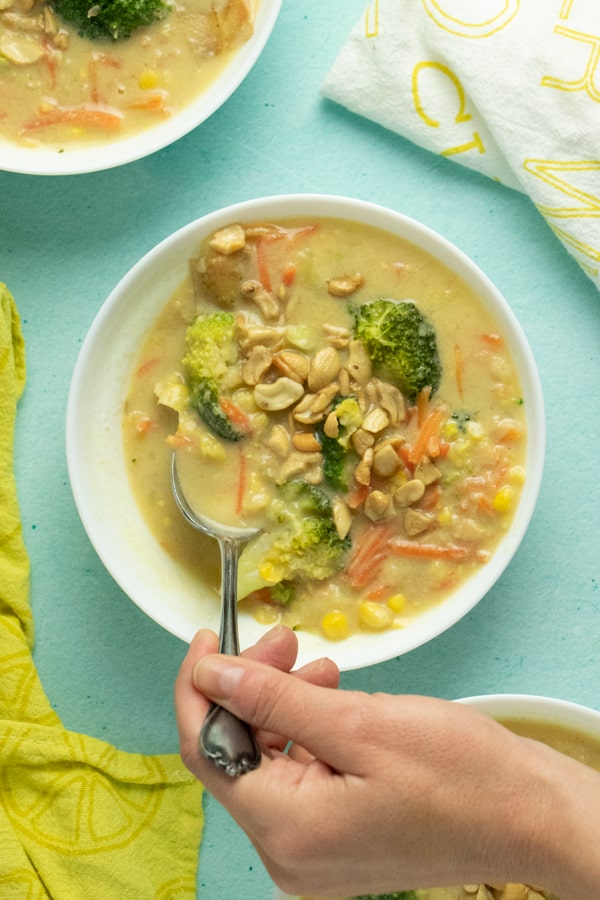 hand using a big spoon to scoop up a bite of vegan corn chowder