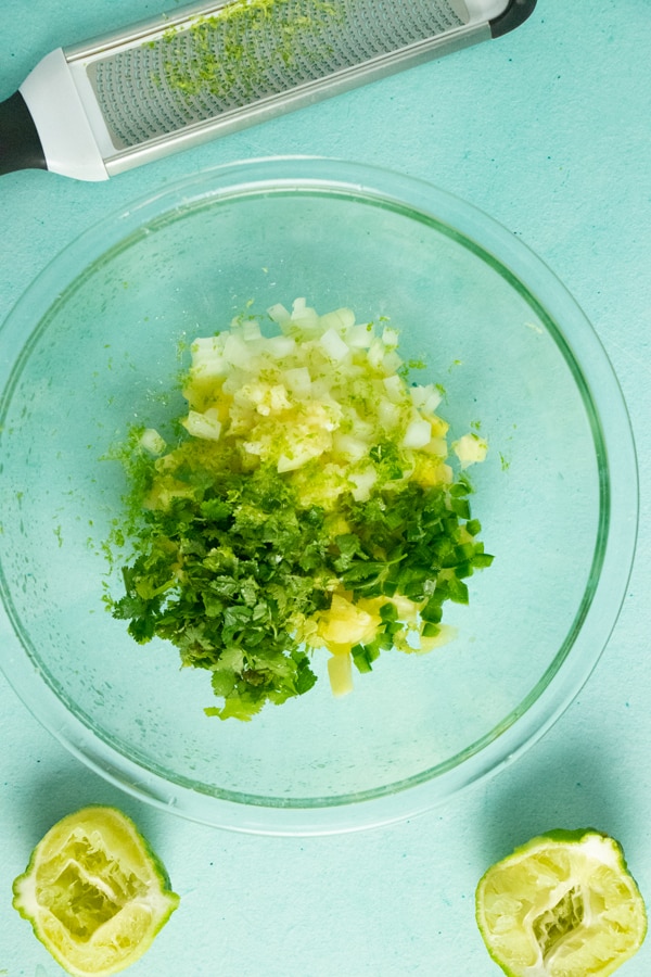 glass bowl of pineapple salsa ingredients before mixing next to squeezed limes and a citrus zester