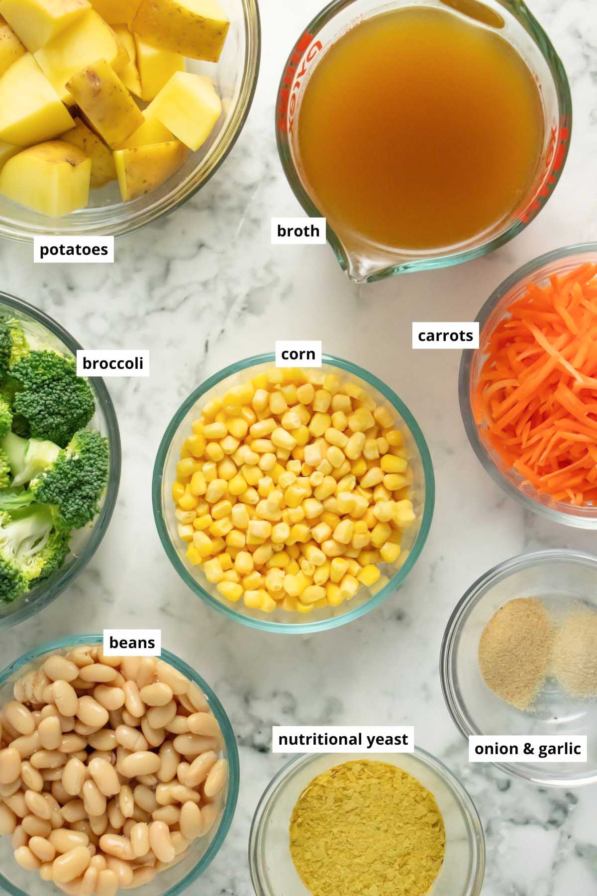 corn, beans, broth, veggies, and seasonings in bowls on a marble countertop