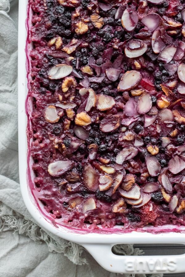 close-up of a pink grain casserole in a white pan with berries, almonds, and millet