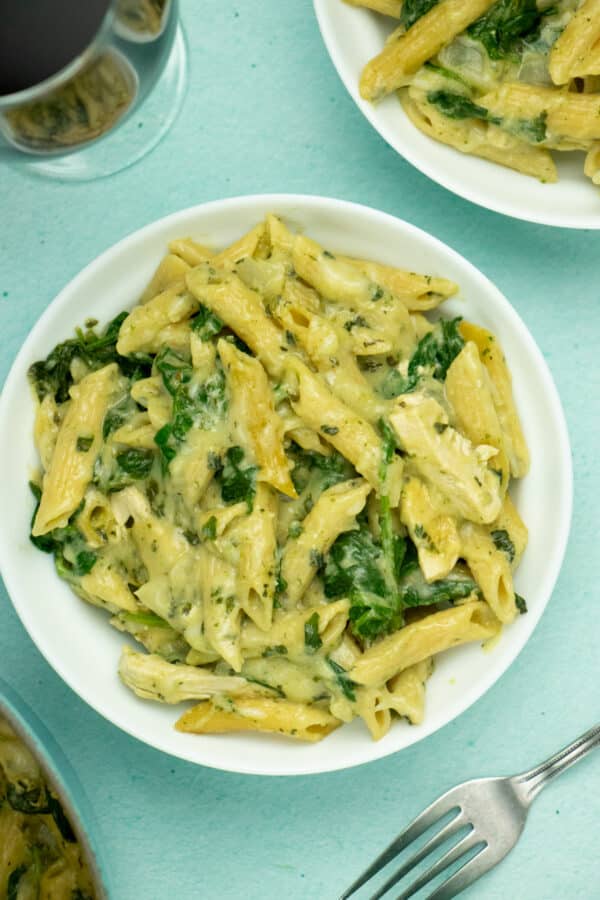 bowl of baked vegan pasta with creamy basil-spinach  sauce on a blue table