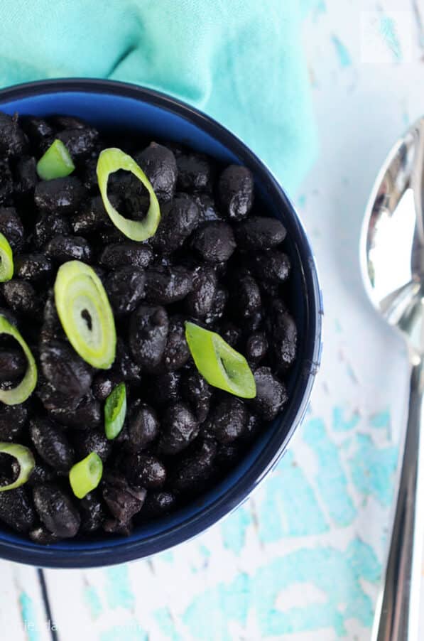 bowl of Instant Pot black beans with green onions on top next to a spoon on a blue table