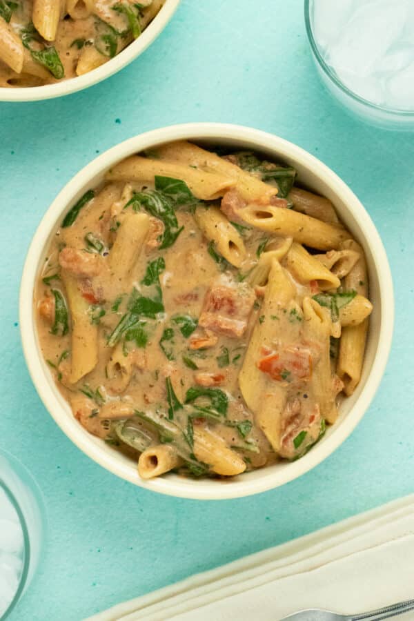 overhead photo of penne in a bowl with creamy tomato spinach sauce