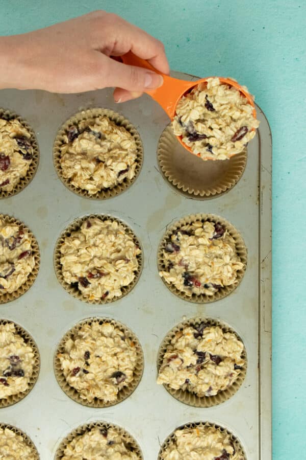 using a ¼ cup measuring cup to scoop oatmeal batter into the lined muffin pan