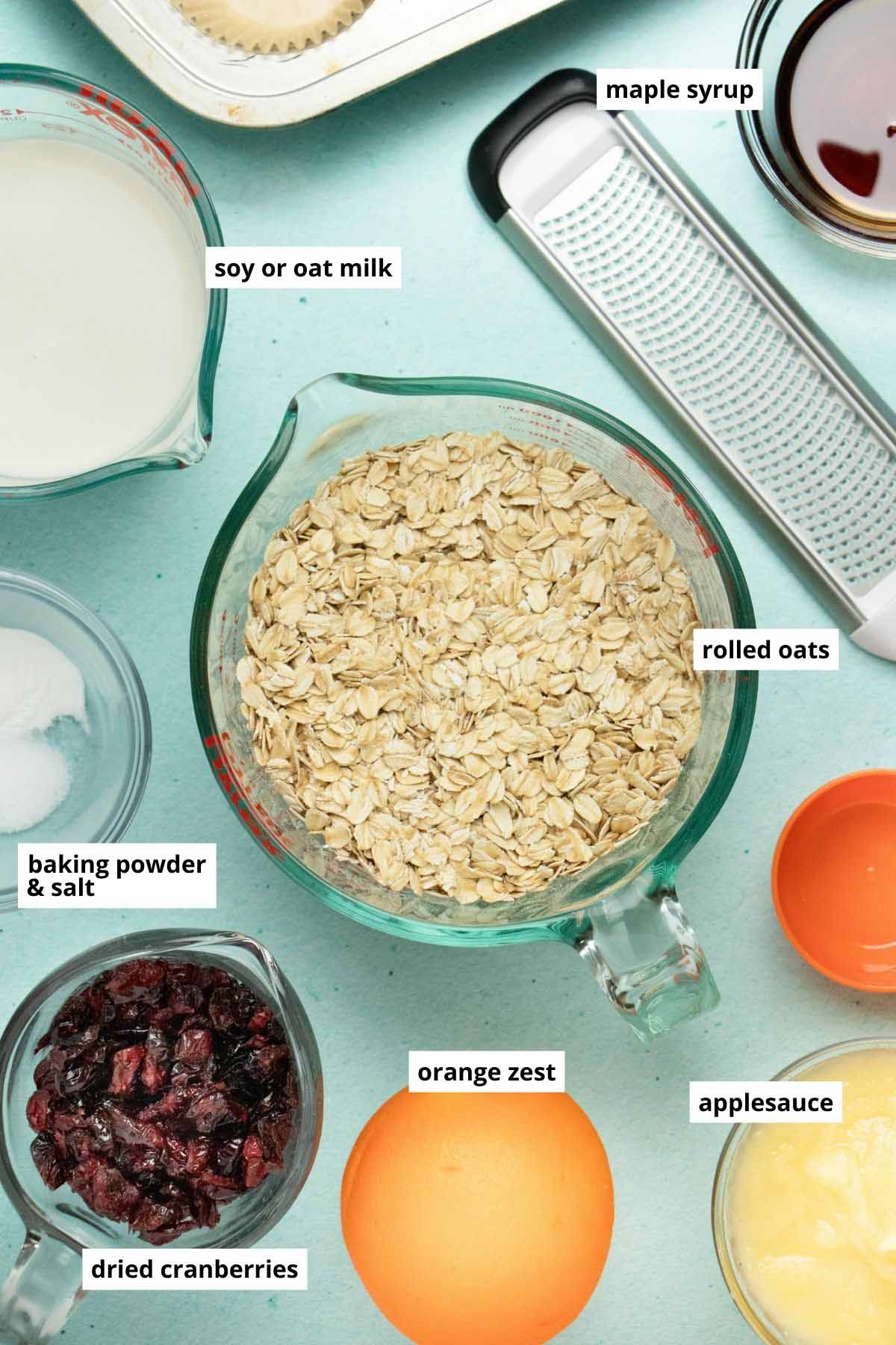 rolled oats, soy milk, applesauce, maple syrup, and other baked oatmeal ingredients in cups on a blue table
