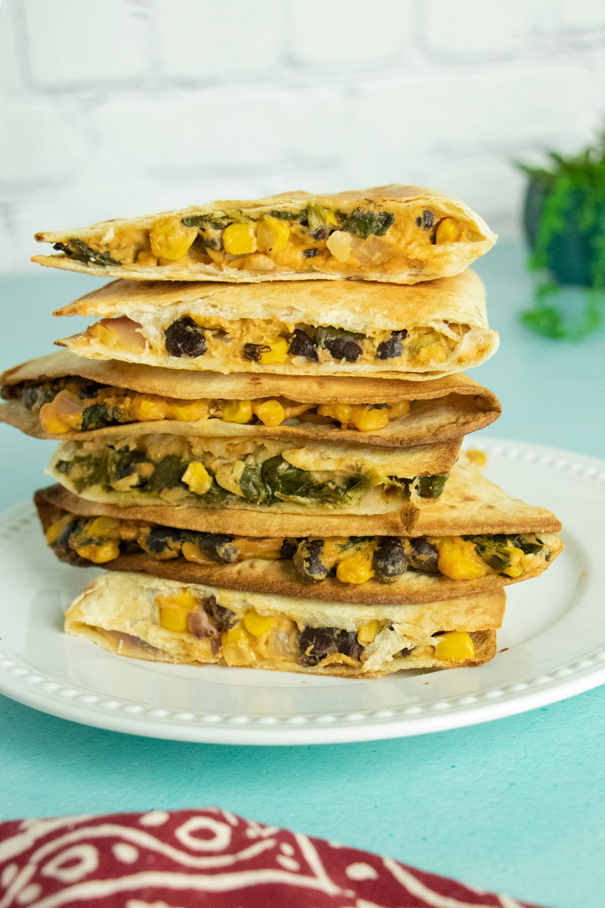 a stack of vegan quesadillas with beans and corn on a white plate