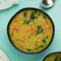 A bowl of yellow split pea soup with carrots and Swiss chard on a blue table