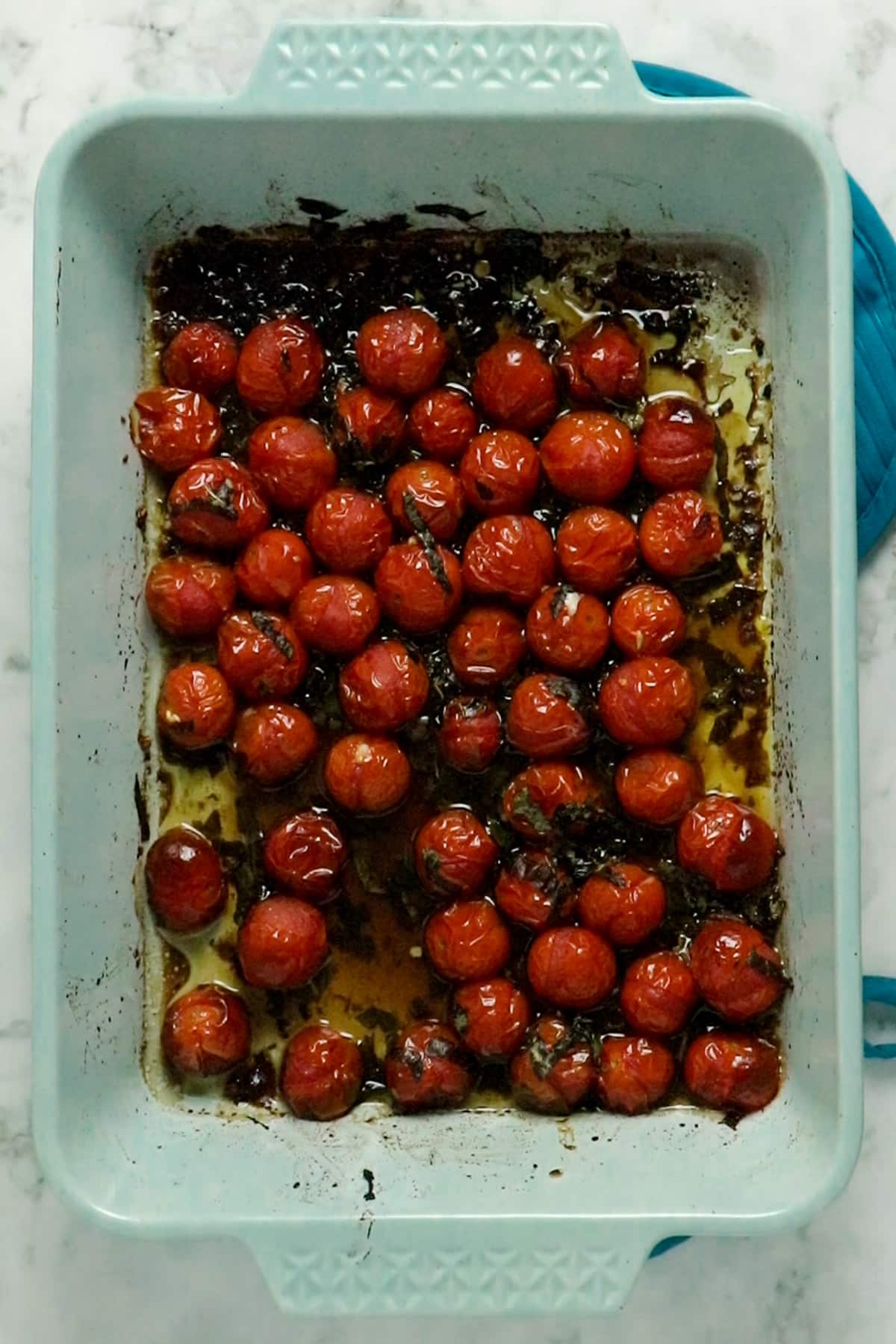 overhead photo of roasted cherry tomatoes in a light blue baking pan