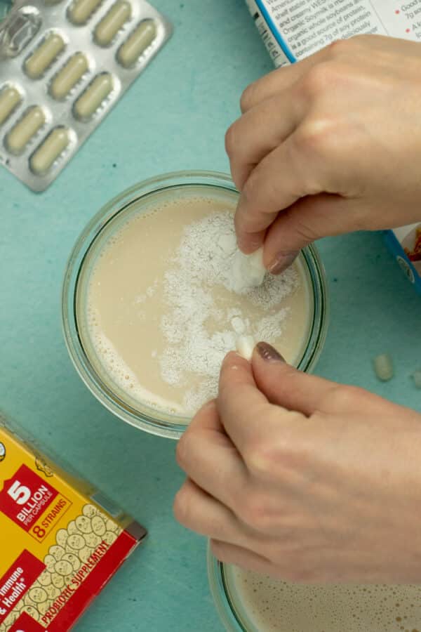 hand breaking open a probiotic capsule into a glass jar of soymilk