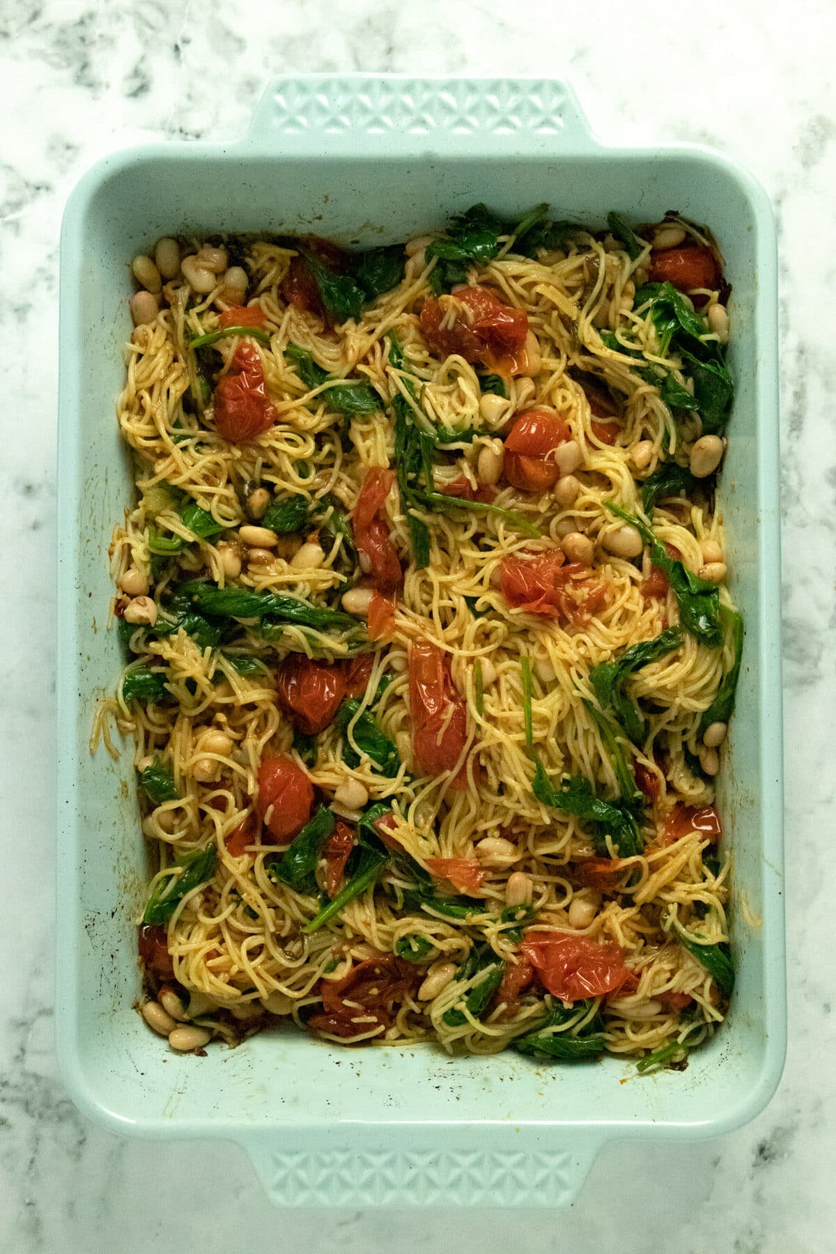overhead photo of roasted cherry tomato pasta with basil, garlic, spinach, and beans in a blue baking pan