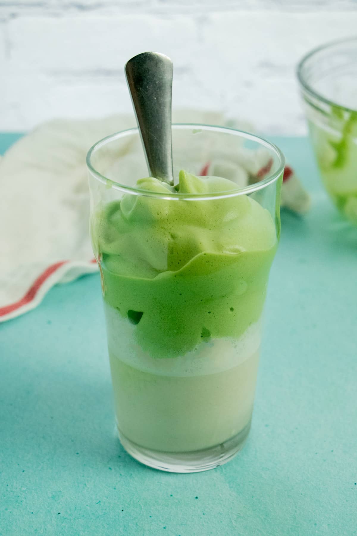 glass of matcha whipped tea spooned over milk in a pint glass on a blue table