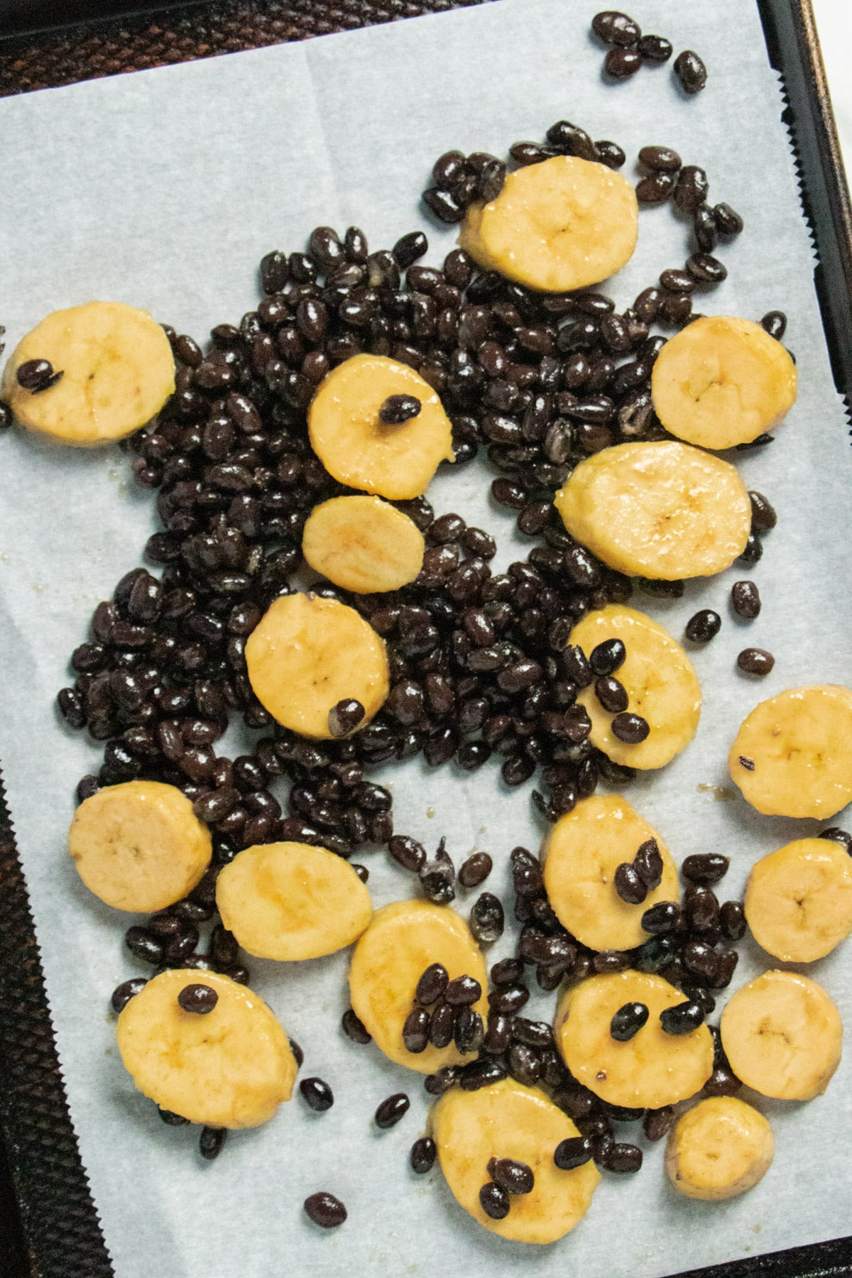 plantains and black beans spread out on a lined baking sheet