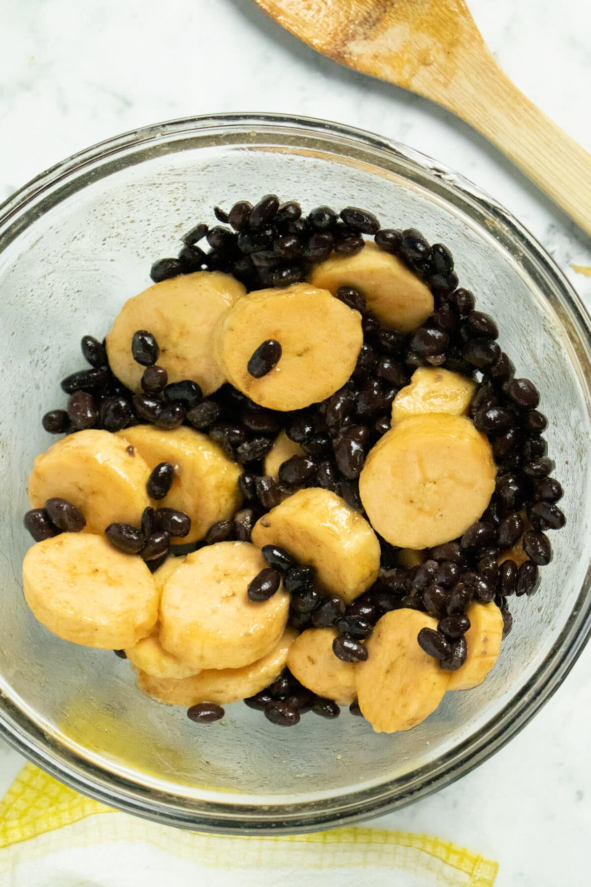 glass mixing bowl of seasoned plantains and black beans, before baking