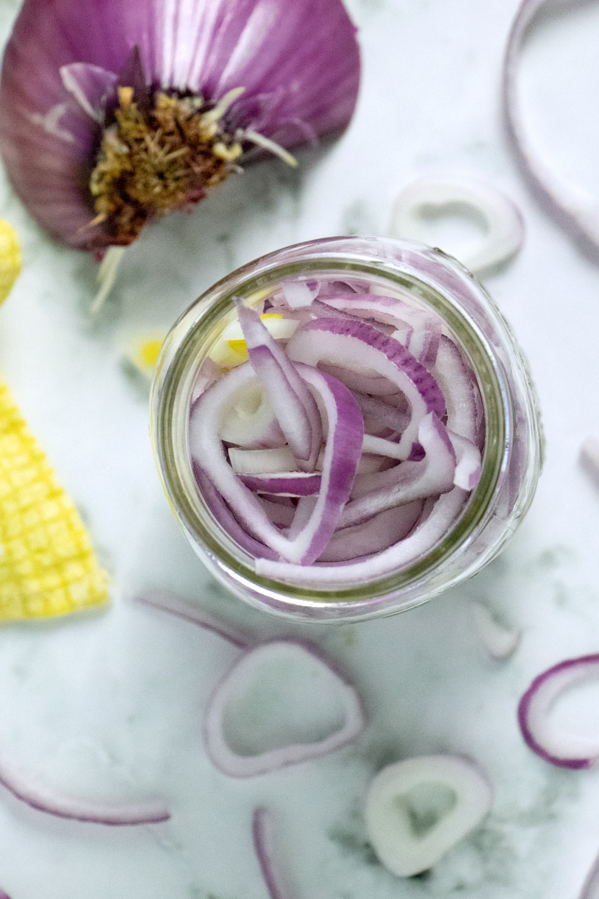 sliced red onion in a mason jar with onion on the table around it