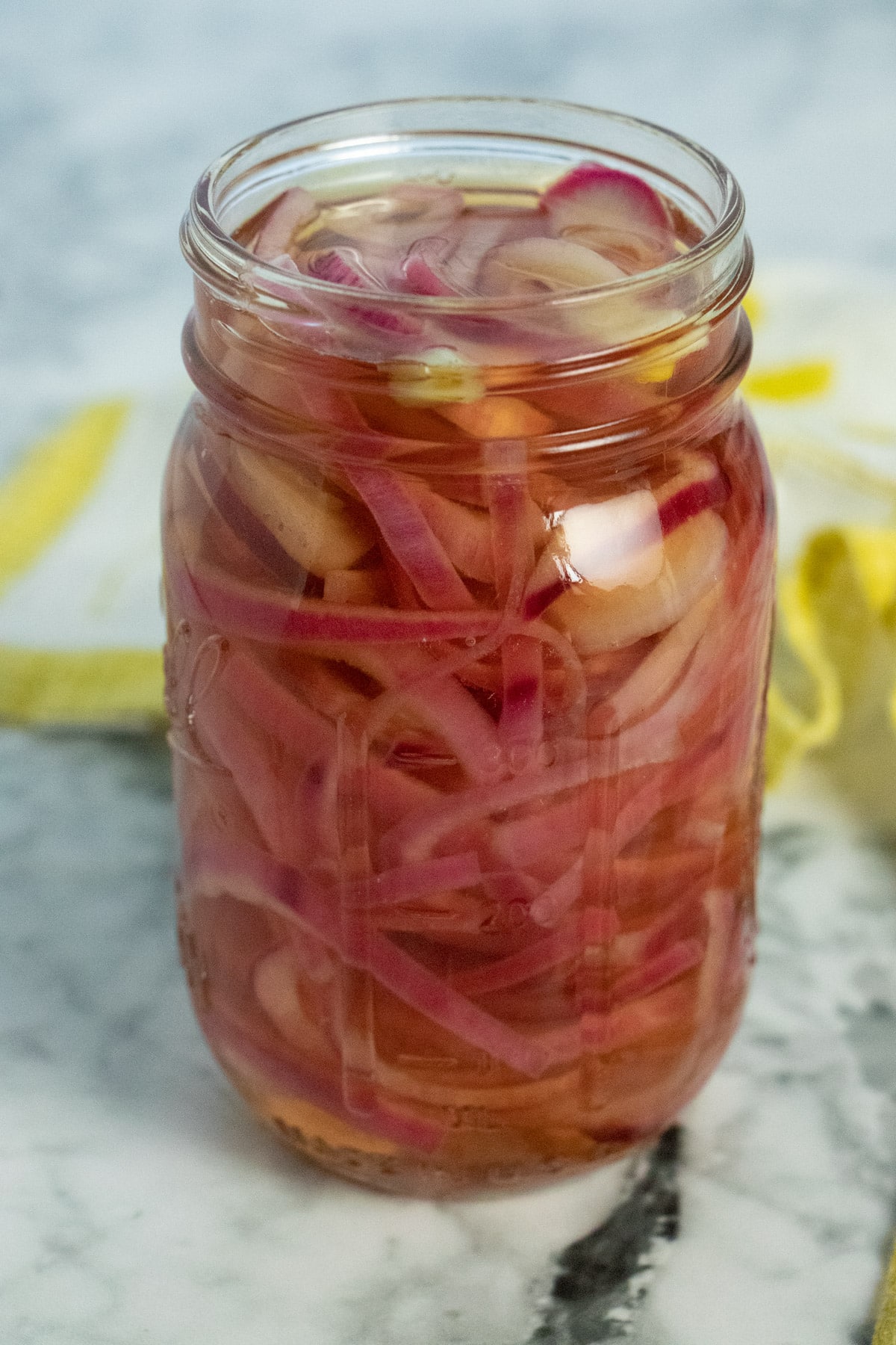 pint jar of sweet pickled onions on a marble tabletop with a yellow and white tea towel in the background