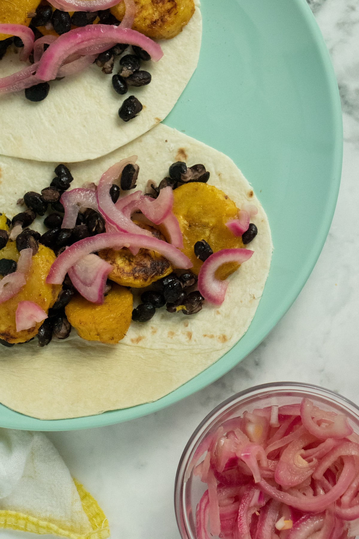 overhead photo of plantain and black bean tacos with sweet pickled onion on top