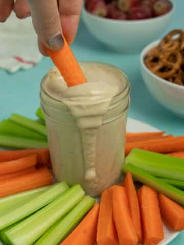 dipping a carrot into a jar of tahini miso dressing, so you can see the creamy texture of the sauce