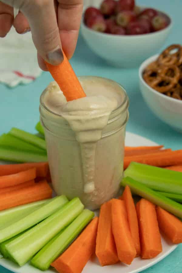 dipping a carrot into a jar of tahini miso dressing, so you can see the creamy texture of the sauce