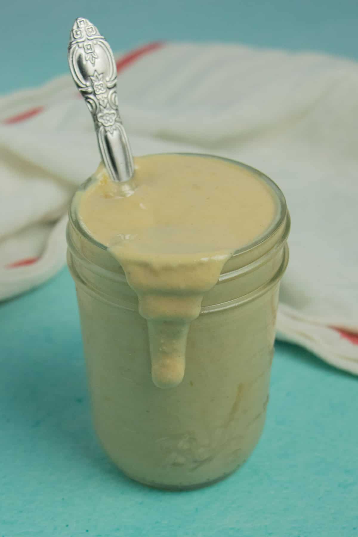 small, glass jar of creamy dressing with a spoon in it and some of the dressing dripping down the side of the jar