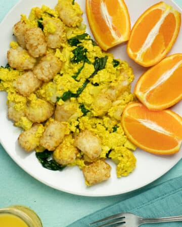 Tofu scramble casserole with tots on a plate next to a side of orange slices
