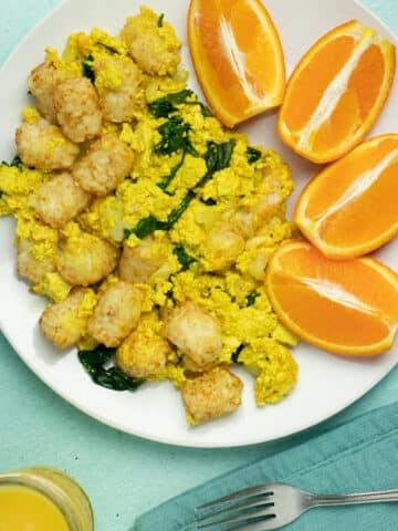 Tofu scramble casserole with tots on a plate next to a side of orange slices