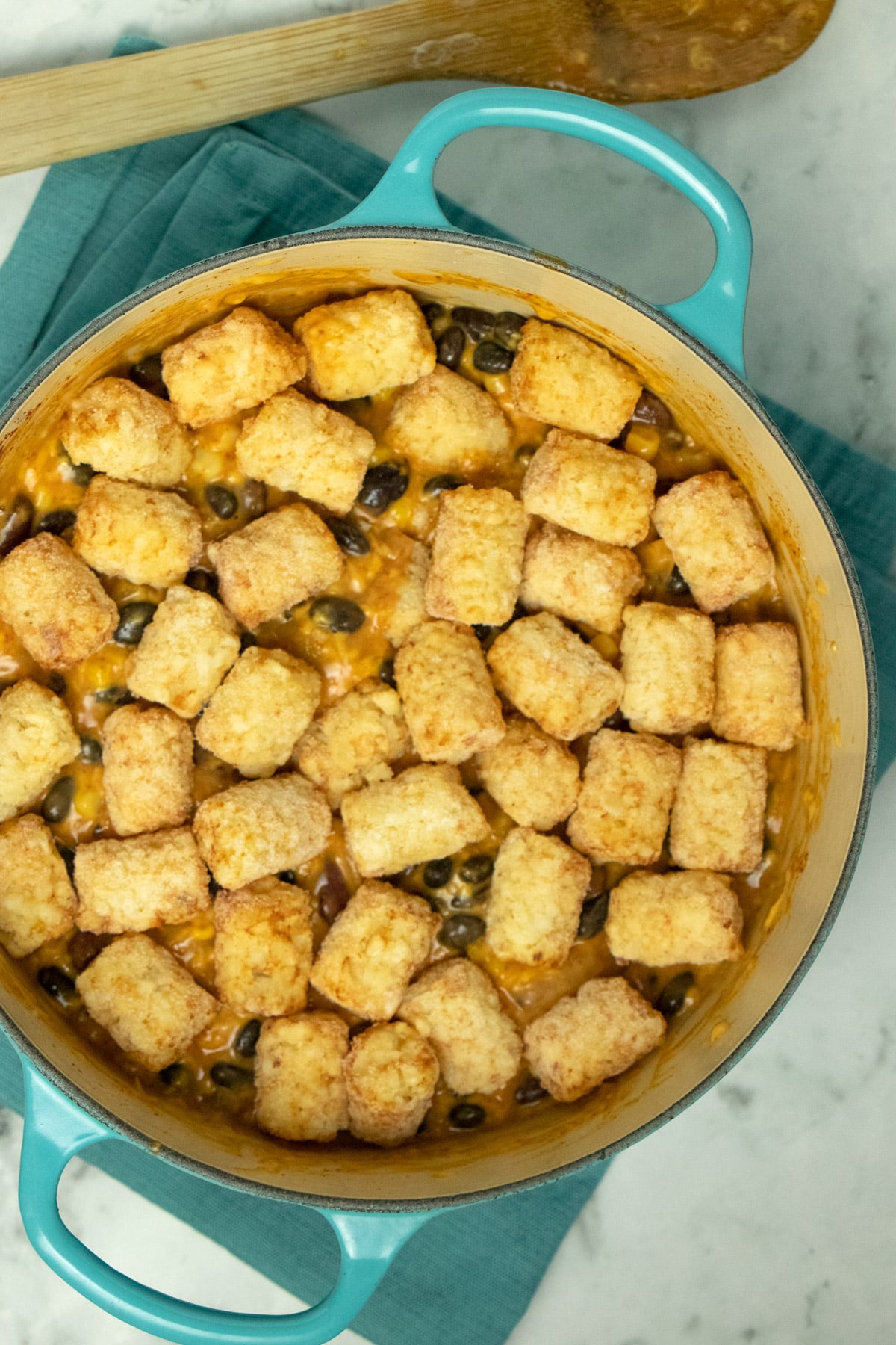unbaked tater tot casserole in a blue pan, so you can see the single layer of tater tots