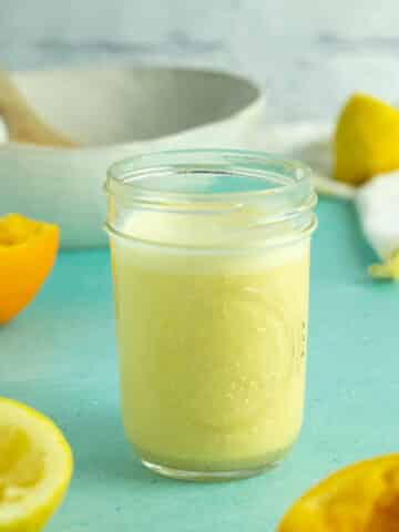 mason jar of citrus dressing on a blue table next to a salad bowl and halved lemons and oranges