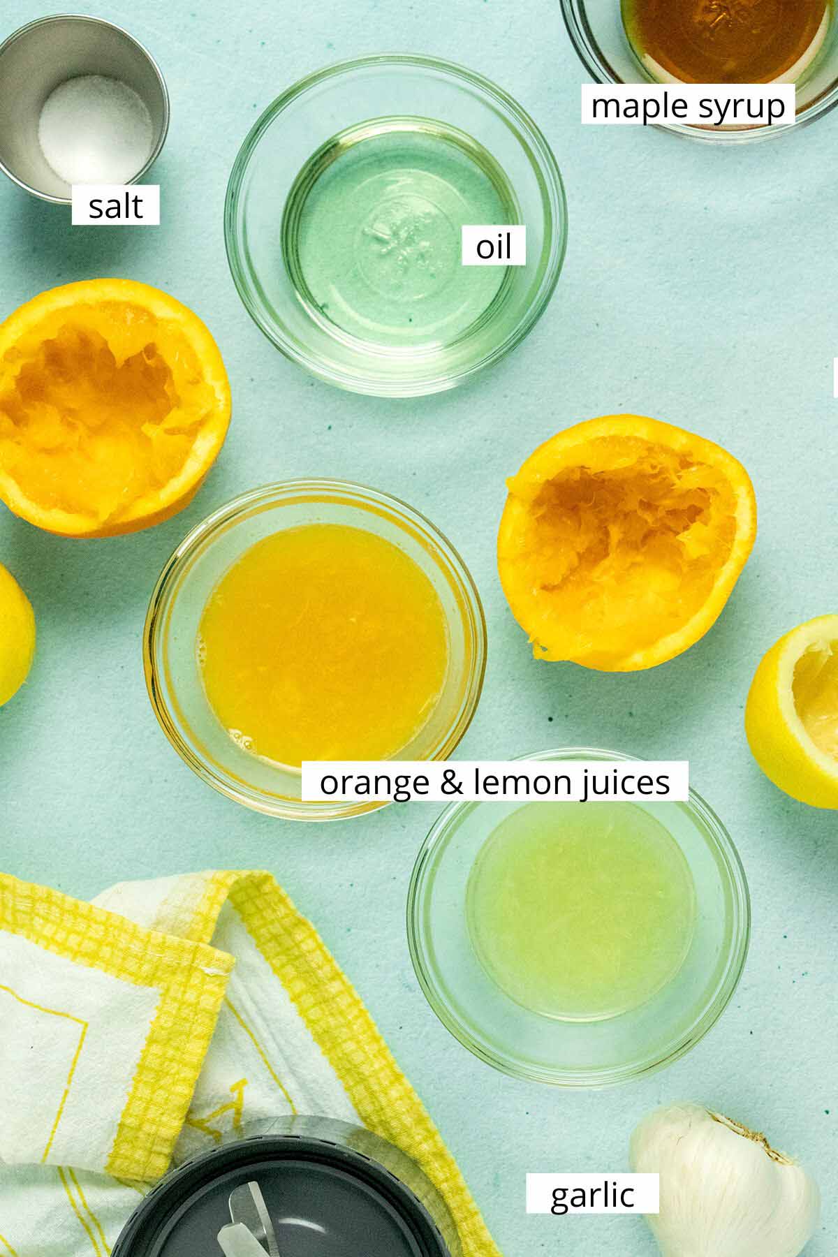 citrus juices, oil, maple syrup, salt, and garlic on a light blue table with text labels on each ingredient