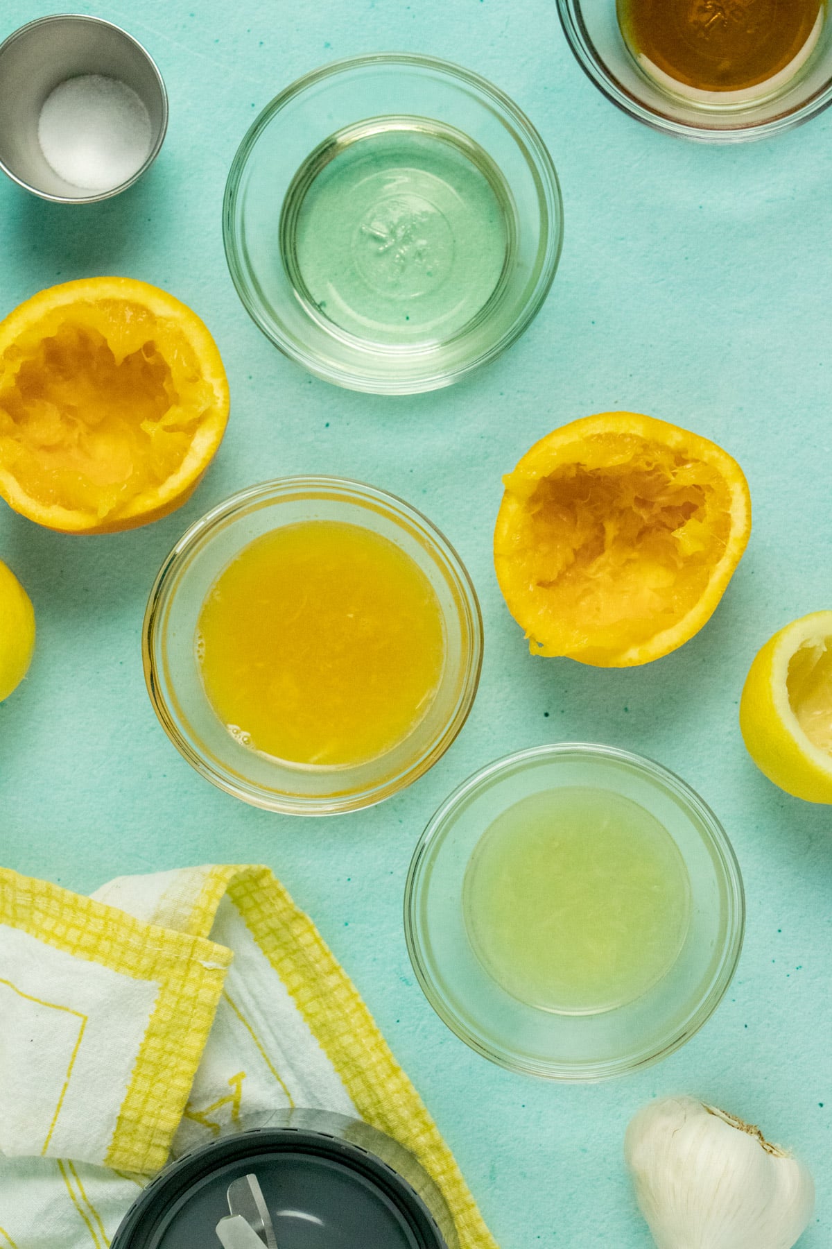 citrus dressing ingredients on a blue table with juiced lemon and orange halves scattered around them
