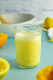mason jar of citrus dressing on a blue table next to a salad bowl and halved lemons and oranges