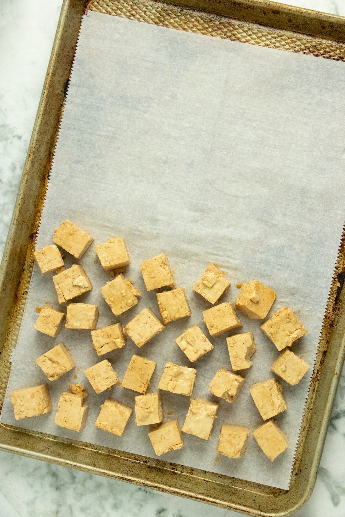 lined baking sheet with marinated tofu arranged in a single layer on one half of it