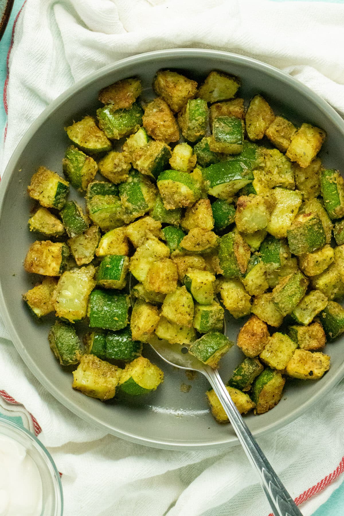 serving platter of cheesy vegan air fryer zucchini with a serving spoon dishing up a scoop