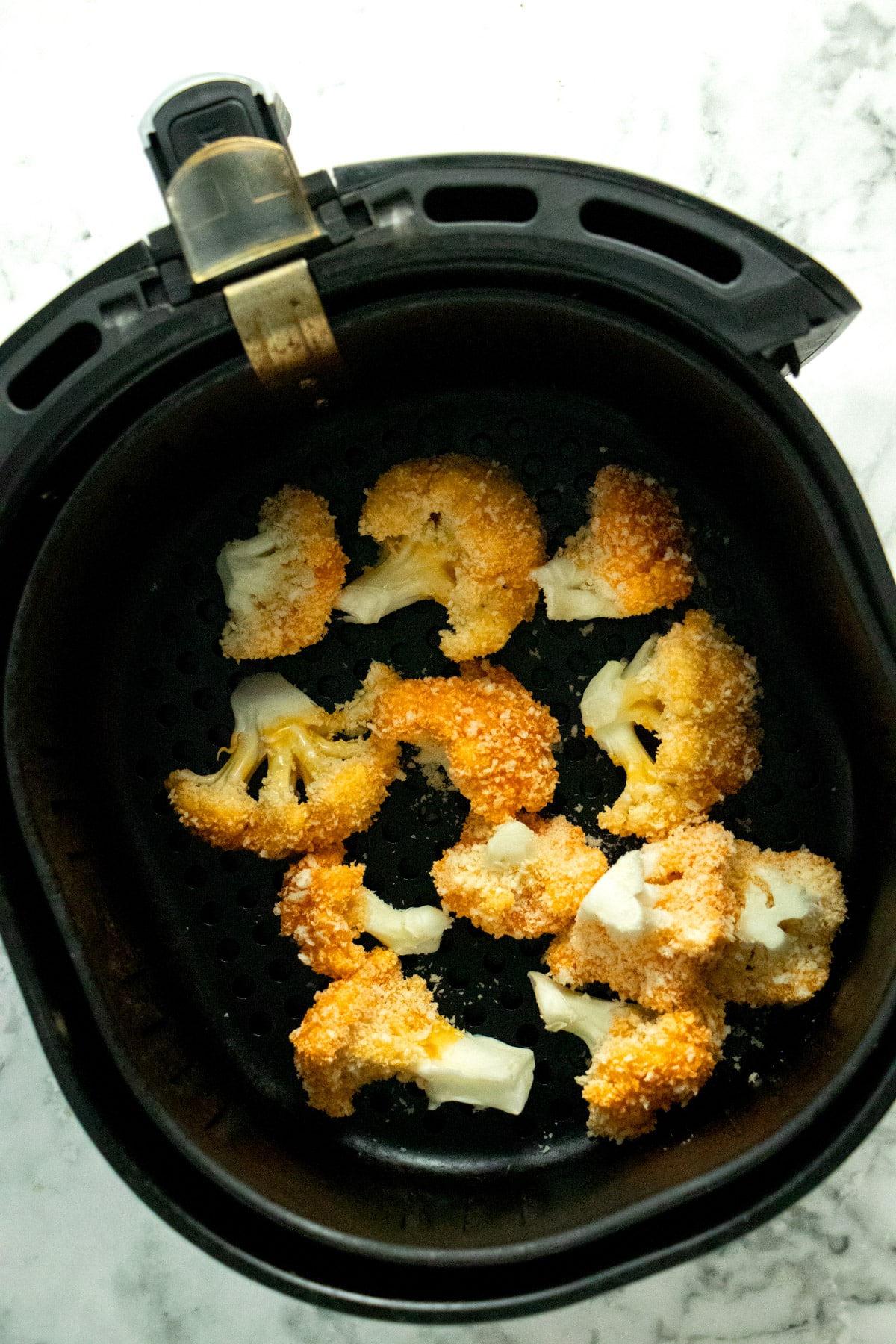 breaded buffalo cauliflower in the air fryer basket before cooking