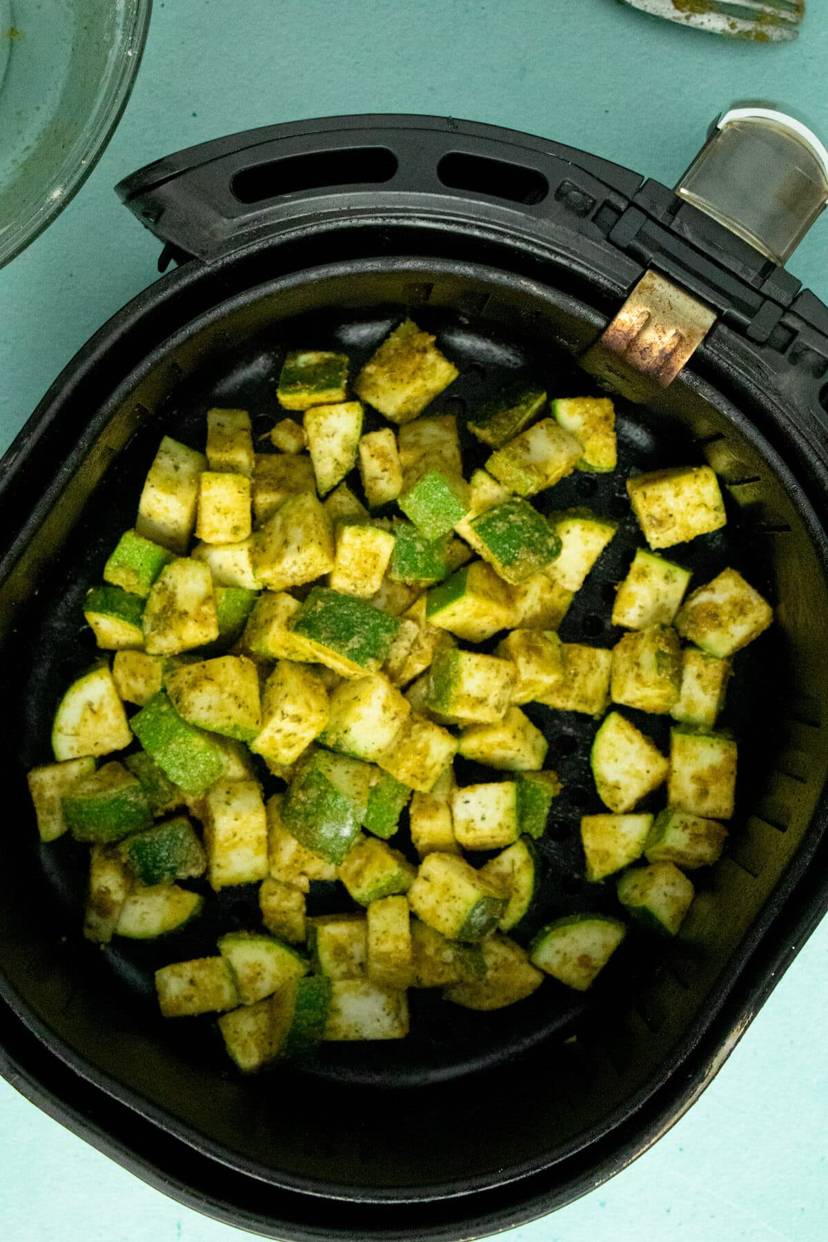 overhead photo of coated zucchini in the air fryer basket on a blue table