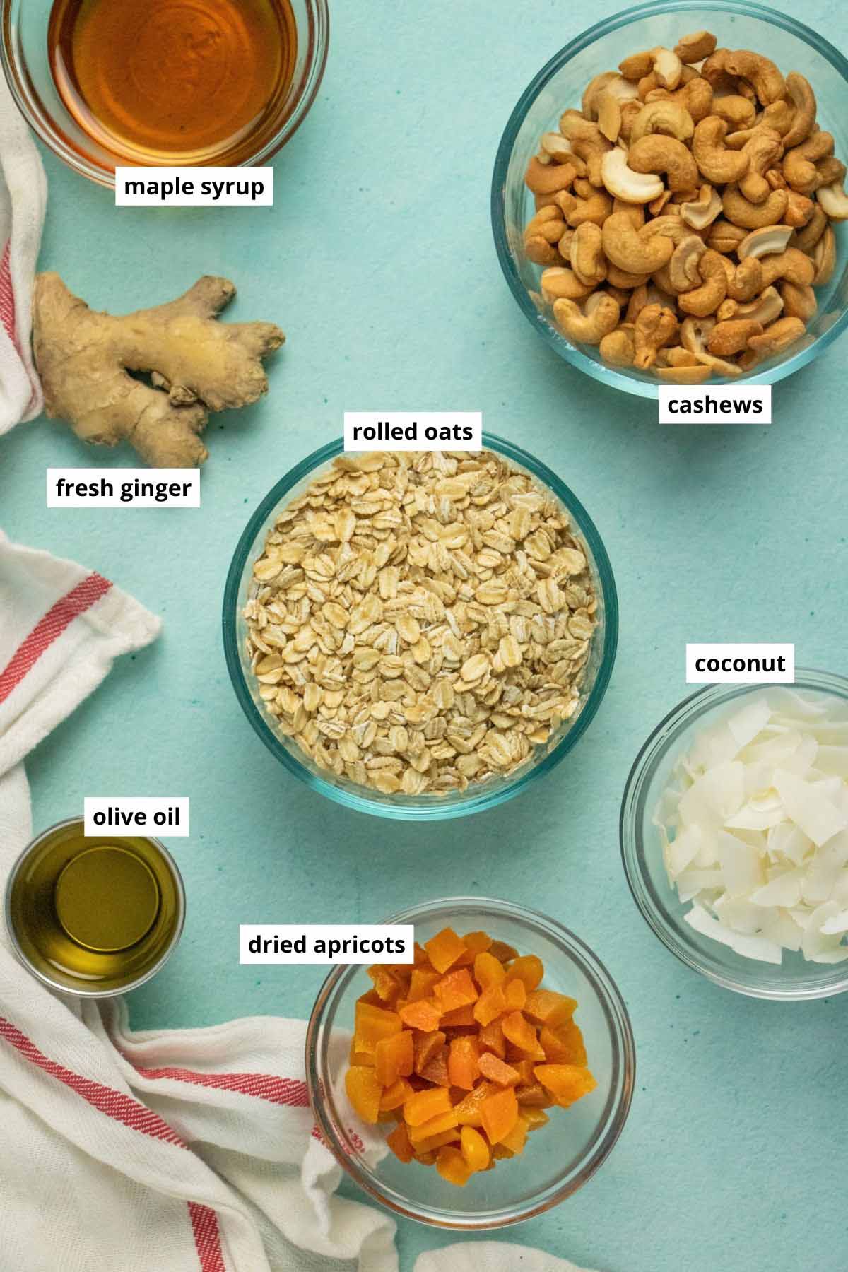 oats, ginger, apricots, and other granola ingredients in bowls on a blue table