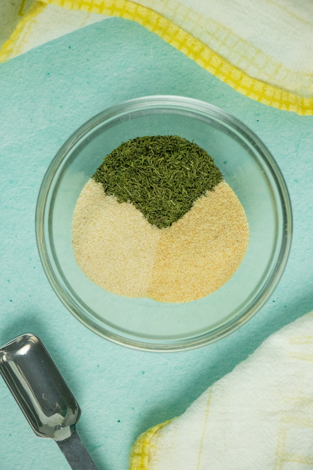 overhead photo of a small bowl with dried dill, garlic powder, and onion powder next to a teaspoon measure