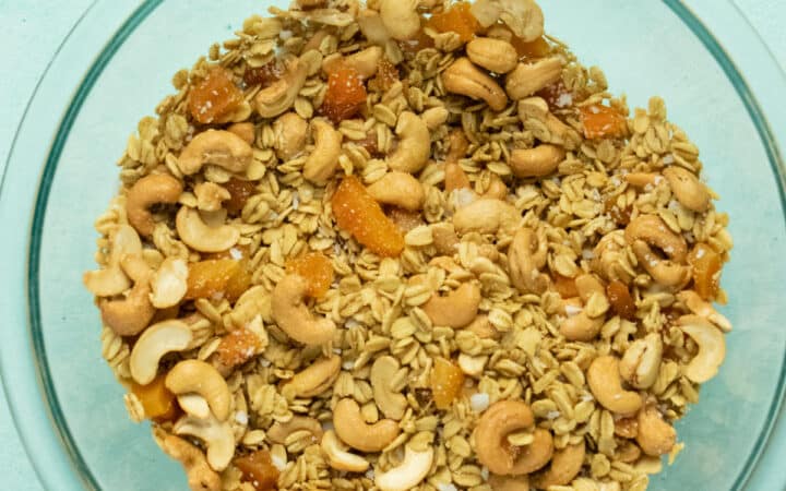 glass mixing bowl of homemade ginger granola with apricots, cashews, and coconut
