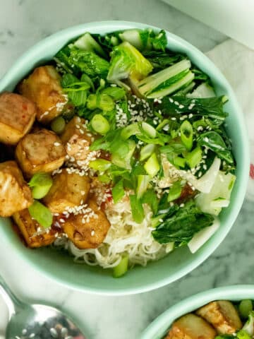 overhead photo of a crispy tofu bowl with bok choy, sweet chili sauce, noodles, sesame seeds, and green onion next to an EZ Tofu Press