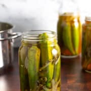 jars of pickled okra on a wooden counter with a marble backsplash